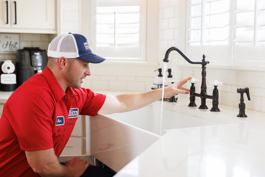 plumber kneeling at sink testing the faucet
