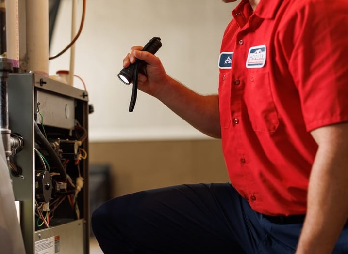 HVAC technician shining flashlight into furnace